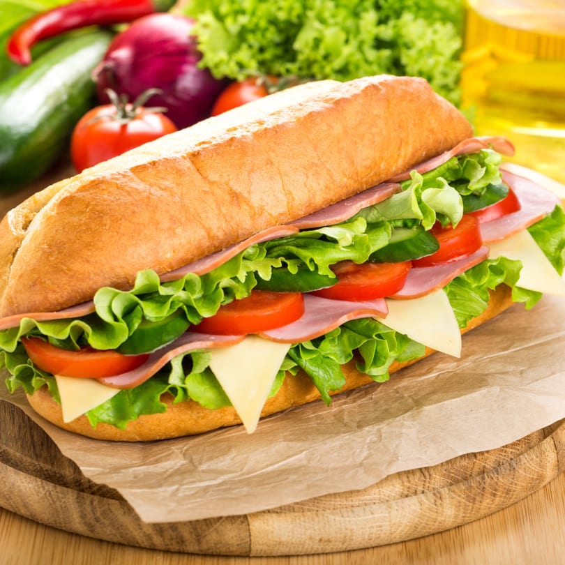 A fresh submarine sandwich with ham, cheese, lettuce, and tomatoes on a wooden board.