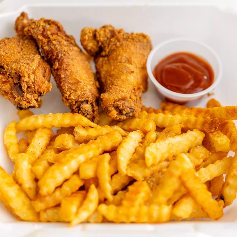 Crispy fried chicken wings and crinkle-cut fries with a side of ketchup in a white takeout container.